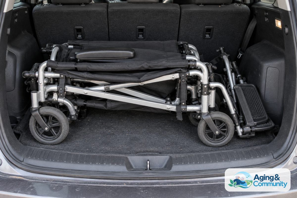 A folded transport chair rests inside an open hatchback cargo area with its small wheels and collapsed seat visible.